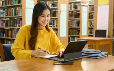 Student girl with tablet in library attending PTE online class