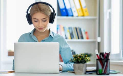 Girl wearing headphone working on laptop for PTE Exam study