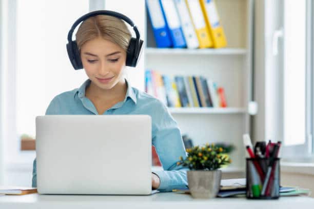 Girl wearing headphone working on laptop for PTE Exam study